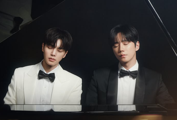 Two men in formal tuxedos and bow ties sit with eyes closed in front of a black grand piano, creating a sophisticated and elegant atmosphere.